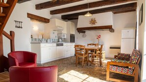 Une cuisine avec des meubles blancs, une table à manger avec des chaises, un canapé rouge et un fauteuil à motifs.