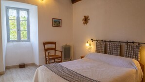 Une chambre à coucher avec un grand lit, une chaise, un radiateur, une fenêtre et un luminaire fixé au mur.
