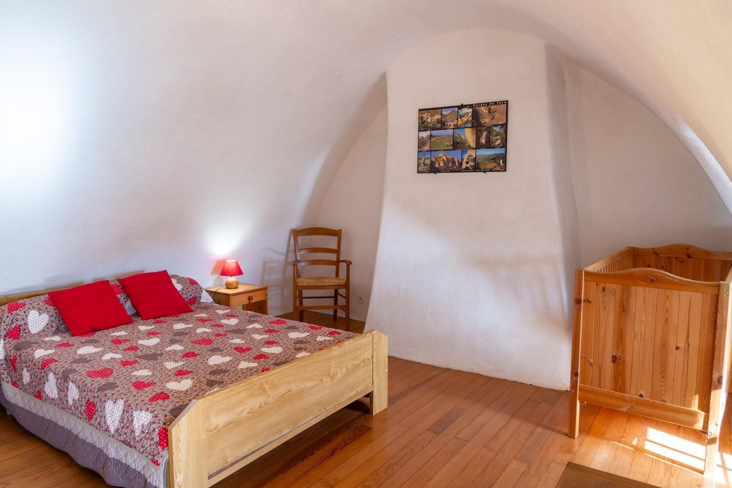 Un dormitorio con una cama de madera, una lámpara roja, una silla de madera y una composición de fotografías colgadas en la pared.