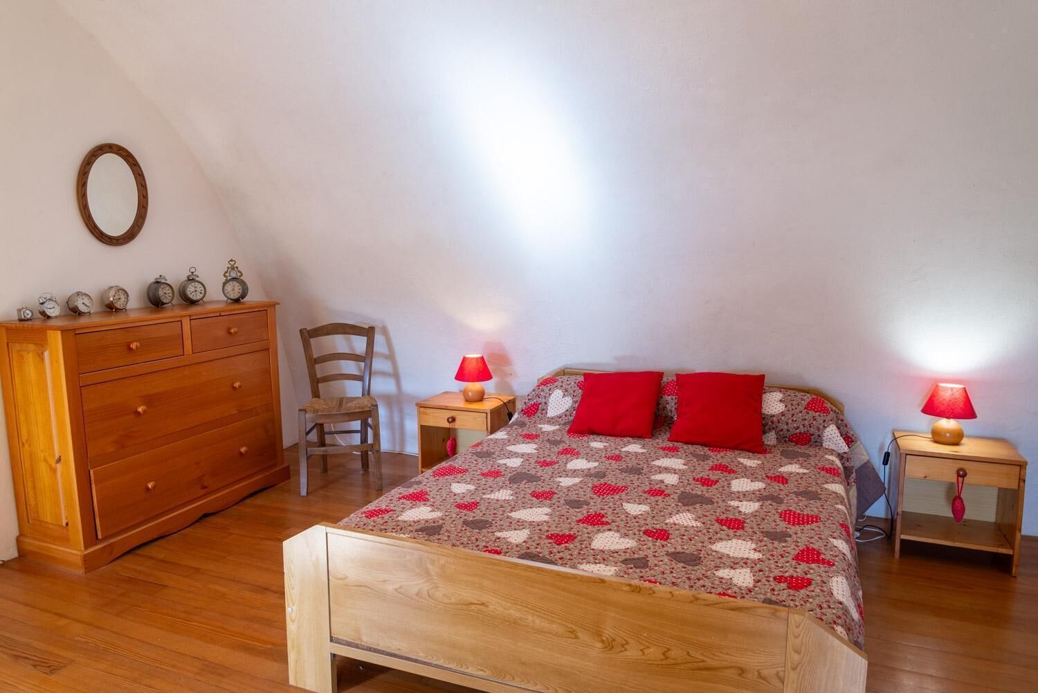 Una camera da letto con un letto in legno, due comodini con lampade, una cassettiera in legno, una sedia e una sveglia a muro.