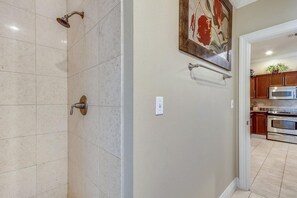 Ein Badezimmer mit Dusche, Toilette und Waschbecken. An der Wand hängt ein Bild und durch eine offene Tür ist eine Küchenzeile erkennbar.