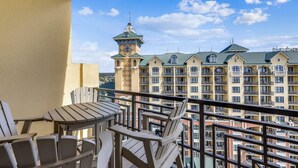 Ein Balkon mit Holzbänken und einem Tisch, mit Blick auf ein Hotel mit mehreren Gebäuden und einem Turm.