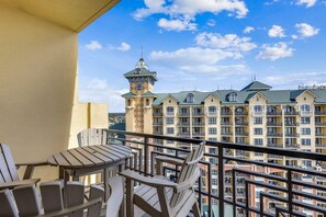 Ein Balkon mit Holzbänken und einem Tisch, mit Blick auf ein Hotel mit mehreren Gebäuden und einem Turm.