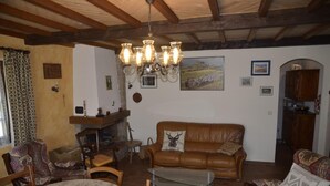 A cozy living room with a brown leather sofa, a glass coffee table, wooden chairs, a fireplace, and a chandelier. - The Parrot in Margeride (PIERREFICHE)