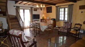 A dining area with a round table, chairs, a chandelier, and a television. - The Parrot in Margeride (PIERREFICHE)