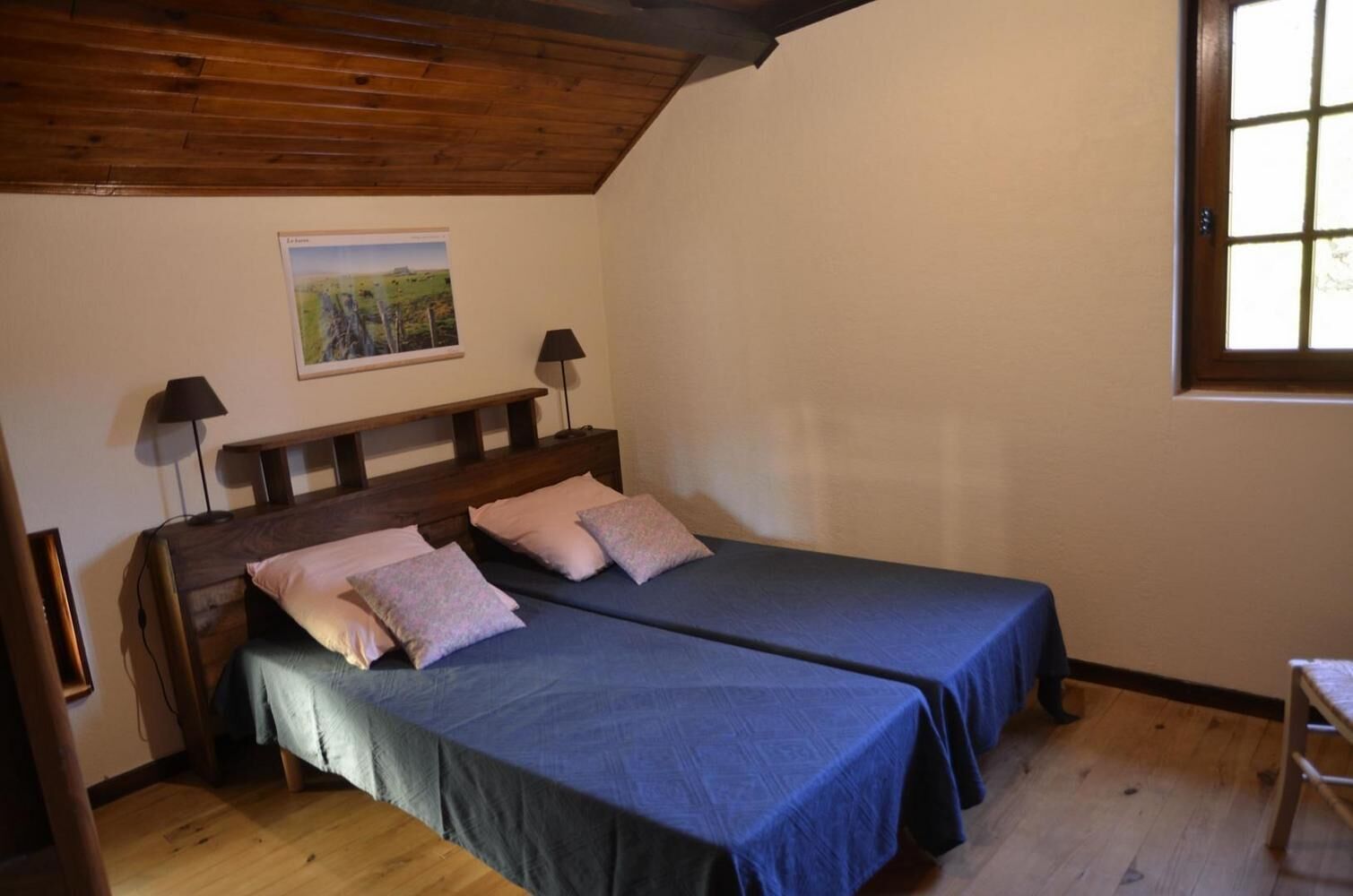 A room with two beds, wooden headboards, a painting on the wall, and a window.