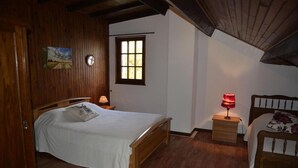 A bedroom with a wooden bed, a bedside table with a lamp, a window, and a door. - The Parrot in Margeride (PIERREFICHE)