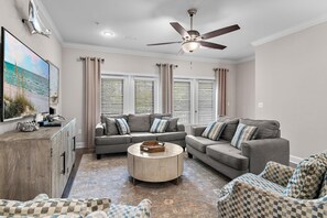 Ein Wohnzimmer mit Deckenventilator, zwei Sofas, einem Couchtisch und einem Fernseher auf einem Holzkasten.