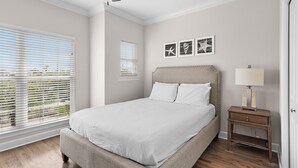 Un dormitorio con cama, mesita de noche, ventilador de techo y dos ventanas con persianas.