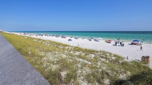 Una playa con arena blanca, agua cristalina y un paseo marítimo pavimentado.