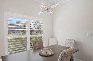 A dining area with a table, chairs, a chandelier, and a view through large windows. - Elegance on the Gulf (Miramar Beach)