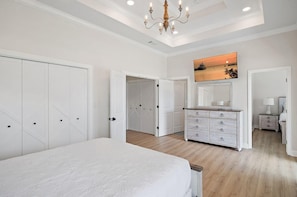 Ein Schlafzimmer mit einem großen Bett, einem Schminktisch, einem Nachttisch, einer Chandelüster und einem Gemälde an der Wand.