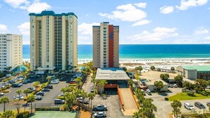 A hotel with a parking lot, a beach view, and a tall building with a red and beige facade. - Destin Towers 122- Destin Dream (Destin)