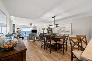 A spacious living area with a dining table, chairs, a television, and a balcony with a view. - Destin Towers 122- Destin Dream (Destin)