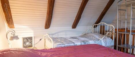 A bedroom with a sloped ceiling, a metal bed frame, a bedside lamp, and a metal shelf unit.