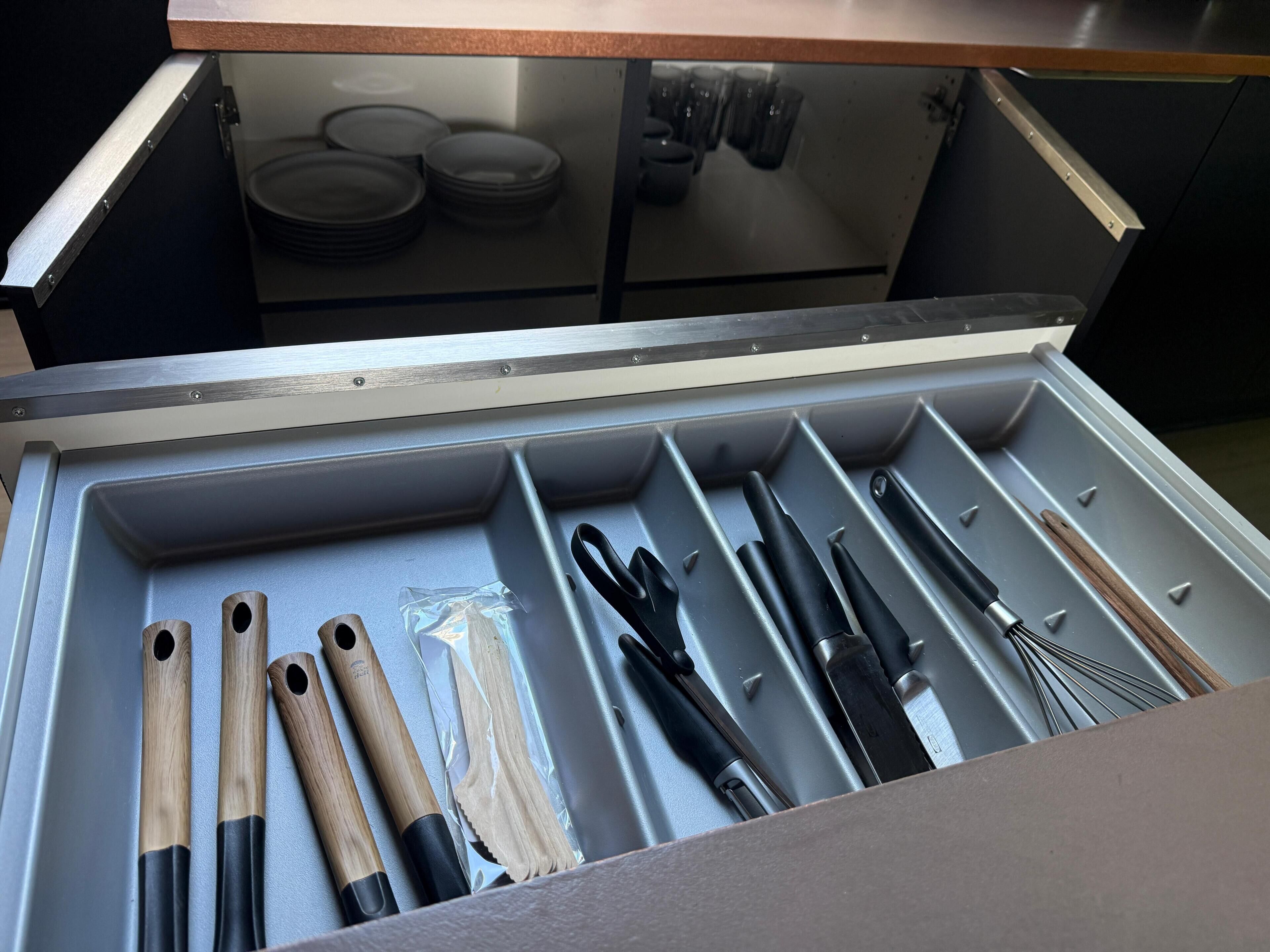 A drawer with kitchen utensils, including knives and wooden spoons.
