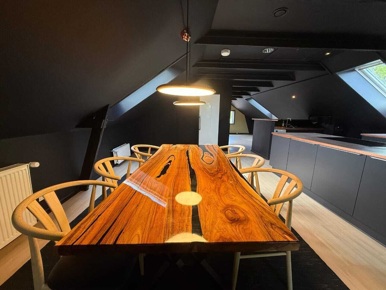 A modern dining area with a wooden table and chairs, a black and white color scheme, and a sloped ceiling with skylights.
