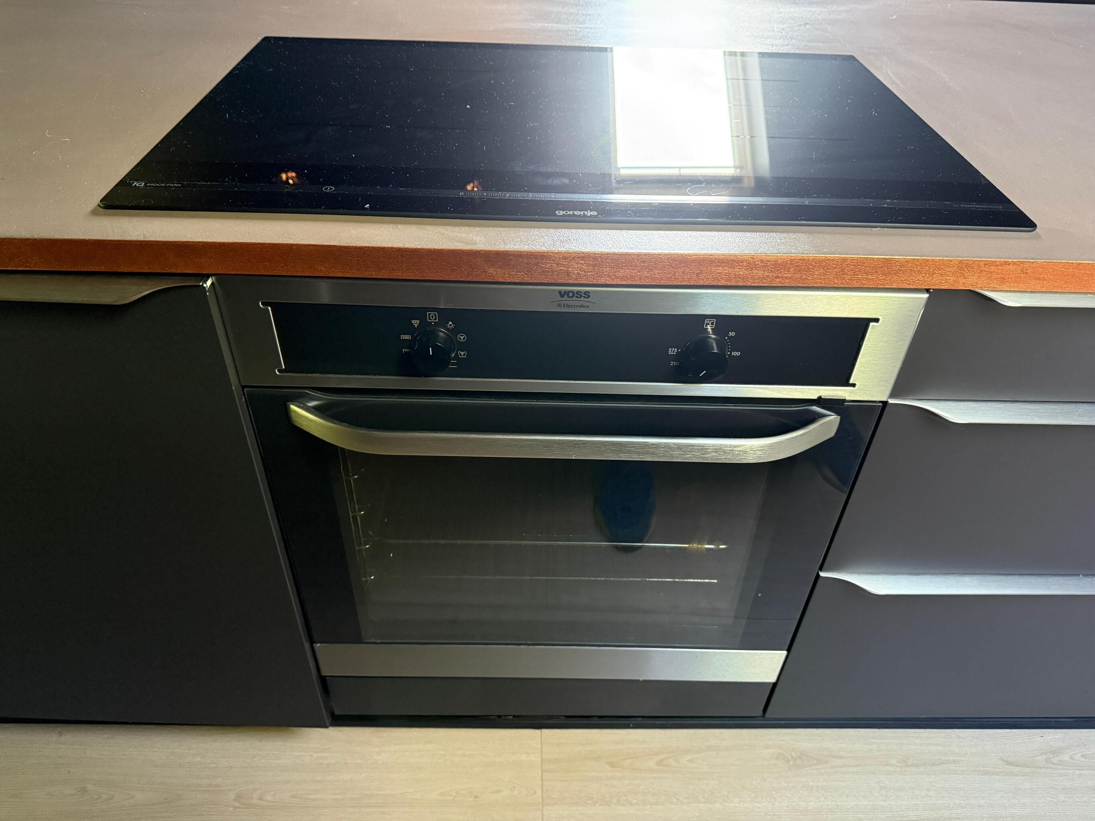 Una cocina con horno empotrado y microondas, encimera de madera y salpicadero de acero inoxidable.