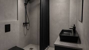 Un baño moderno con cabina de ducha de vidrio, inodoro negro y lavamanos minimalista.
