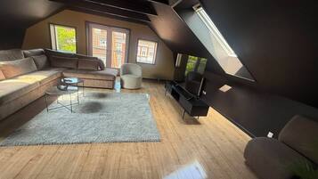 A modern loft-style living room with a sloped ceiling, a large sofa, a coffee table, a TV stand, and a small chair.
