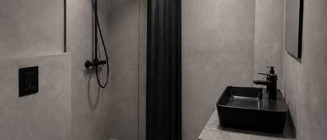 Un baño moderno con ducha de vidrio, inodoro negro y lavamanos con lavabo negro.