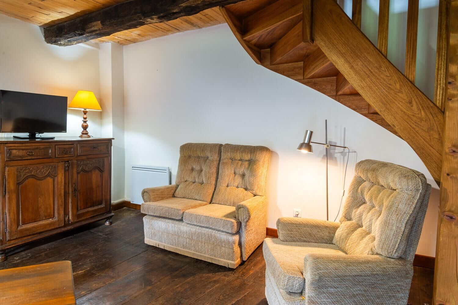 Una sala acogedora con una escalera de madera, un televisor, una lámpara y un sofá.