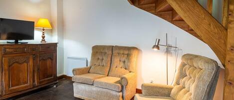 Una sala acogedora con una escalera de madera, un televisor, una lámpara y un sofá.