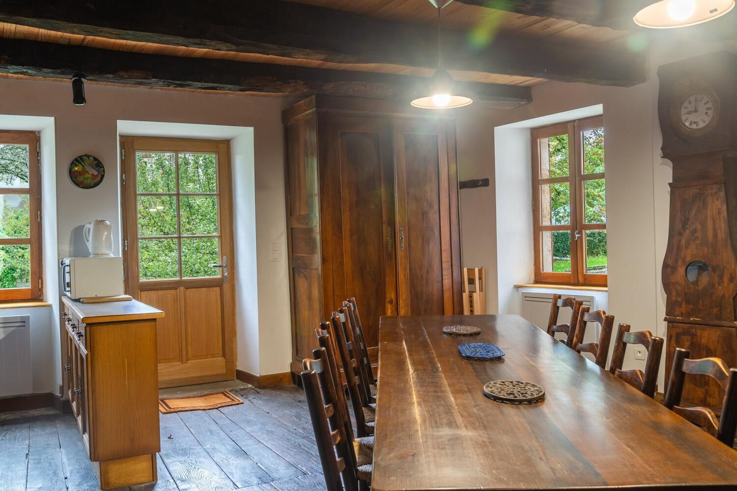 Un comedor con una larga mesa de madera, sillas y un mueble de madera con una tetera.