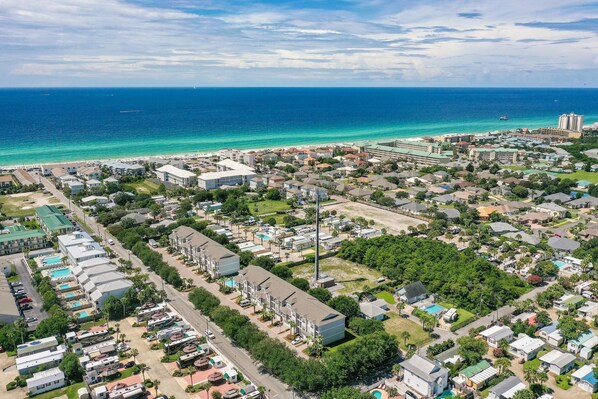 An aerial view of a coastal residential area with houses, a beach, and a clear sky. - Driftwood Townhomes #1- Beachwaves (Miramar Beach)