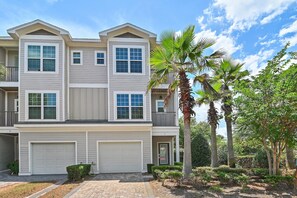 A multi-story residential building with a garage, balconies, and a well-maintained garden with palm trees. - Driftwood Townhomes #1- Beachwaves (Miramar Beach)