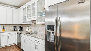 A kitchen with white cabinets, a stainless steel refrigerator, a water dispenser, and a granite countertop. - Driftwood Townhomes #1- Beachwaves (Miramar Beach)