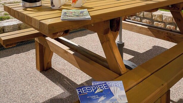 Ein Holztisch für ein Picknick mit einem gelben Sonnenschirm, einem Wasserkocher und Tassen darauf.