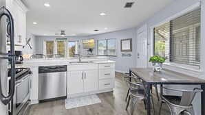 A modern kitchen with white cabinets, a dishwasher, and a dining area with a table and chairs. - Crystal Village II 8B- Vitamin Sea (Miramar Beach)