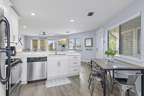 A modern kitchen with white cabinets, a dishwasher, and a dining area with a table and chairs. - Crystal Village II 8B- Vitamin Sea (Miramar Beach)