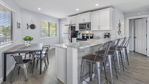 A modern kitchen with white cabinets, a central island with bar stools, a microwave, and a stove. - Crystal Village II 8B- Vitamin Sea (Miramar Beach)