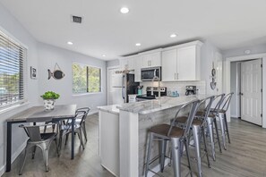 A modern kitchen with white cabinets, a central island with bar stools, a microwave, and a stove. - Crystal Village II 8B- Vitamin Sea (Miramar Beach)