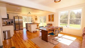 Una cocina moderna con electrodomésticos de acero inoxidable, una zona de comedor con mesa y sillas de madera, y amplios ventanales con vistas al exterior.