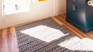 Una habitación con techo inclinado, una ventana con vistas, un armario oscuro, un espejo y una alfombra estampada.