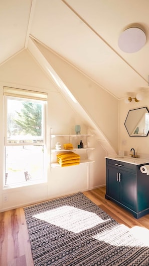 A room with a sloped ceiling, a window with a view, a dark cabinet, a mirror, and a patterned rug.