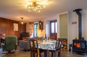 Ein gemütliches Wohnzimmer mit Kamin, einem Esstisch für zwei Personen, einem grünen Sessel und einem Fernseher.