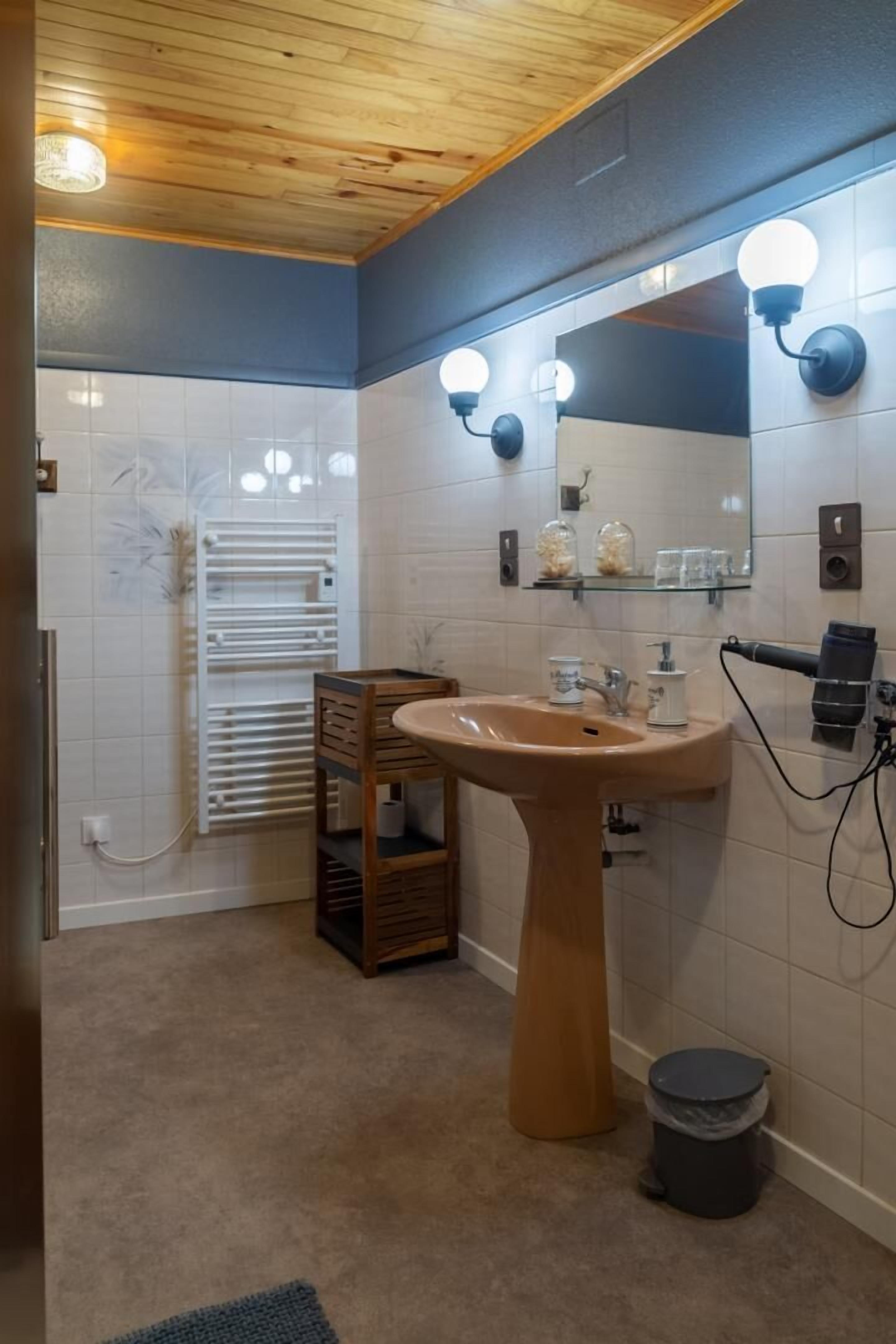 A bathroom with a wooden vanity, a sink, a mirror with lights, a towel rack, and a shower area.