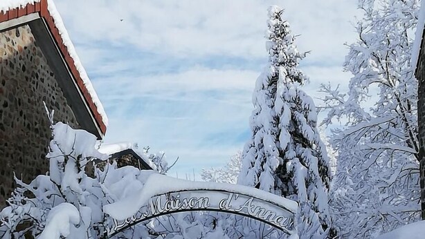 Une porte d’entrée recouverte de neige, sur laquelle on peut lire l’inscription « Maison d’Anna », et un bâtiment en pierre situé à gauche.