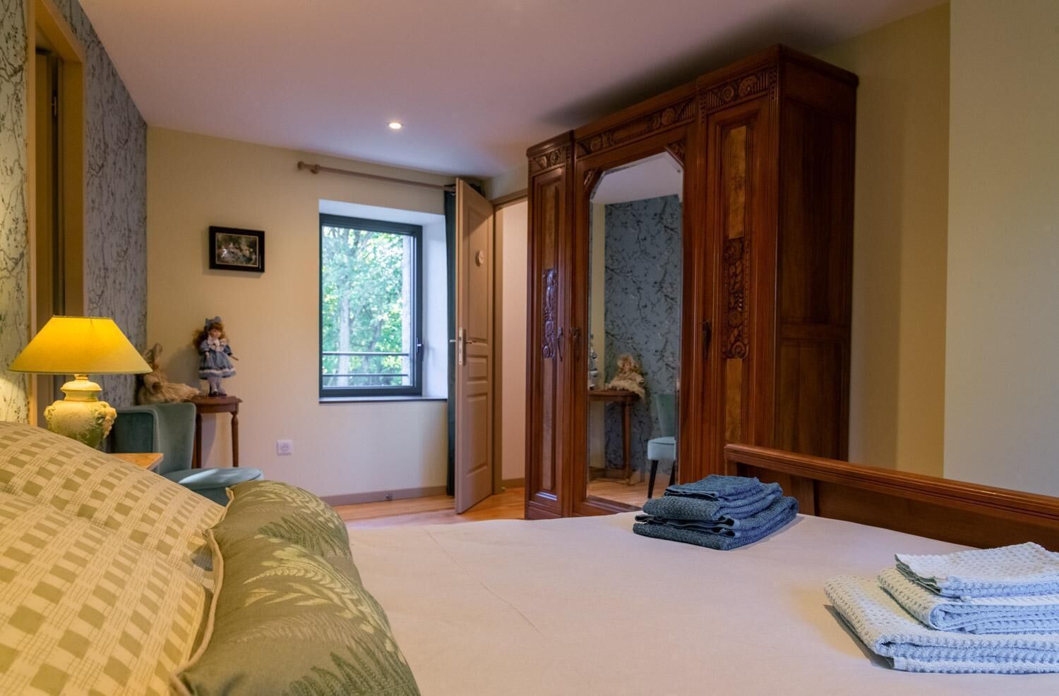 Ein Schlafzimmer mit einem Bett, einer Lampe, einem Schminktisch, einem Fenster und einer Tür zu einem anderen Raum.