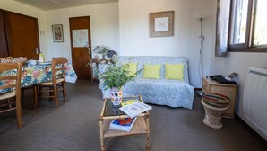 A cozy living room with a sofa, a dining table with chairs, a coffee table with magazines, and a window with blinds. - Chalet Gré, between greenery and Cevennes mountains (LE POMPIDOU)