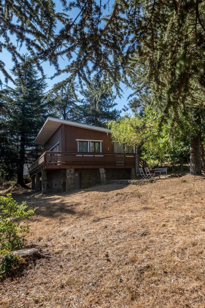 A modern two-story cabin with a balcony, surrounded by dense forest.