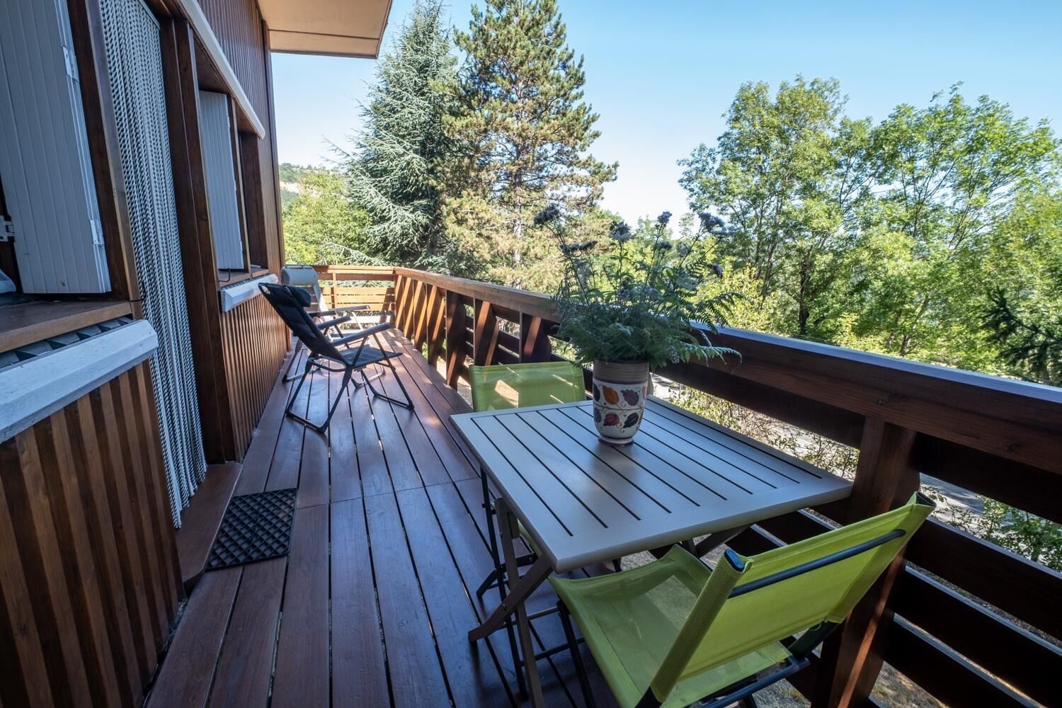 A wooden deck with outdoor furniture, including chairs and a table, and a potted plant.