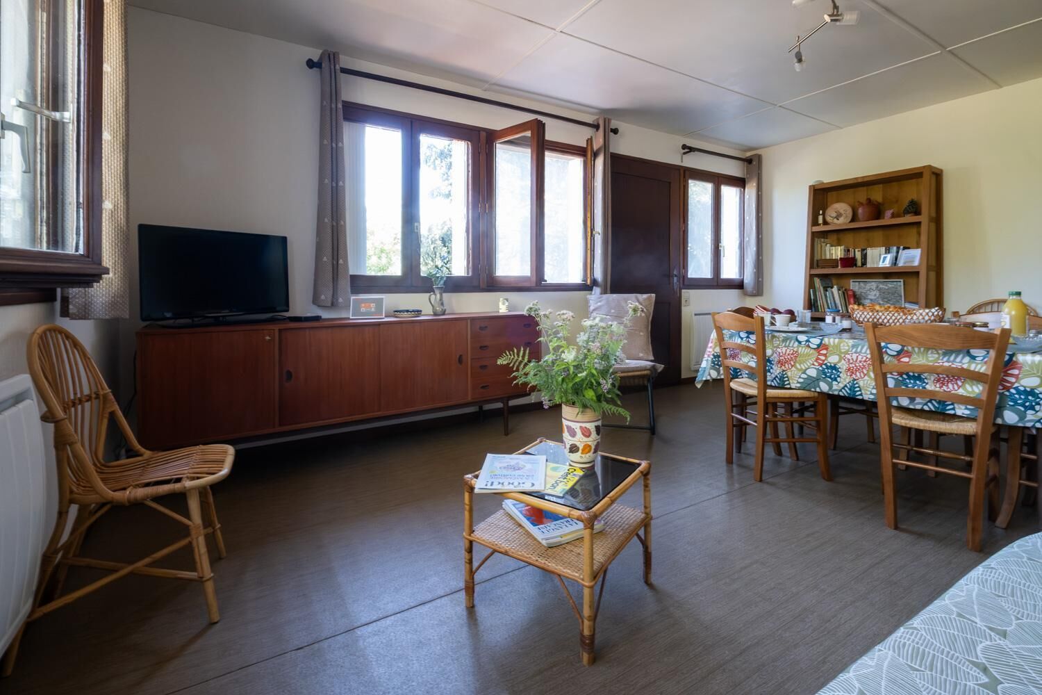 Un salon avec un téléviseur, un coin repas avec une table et des chaises, et une bibliothèque.
