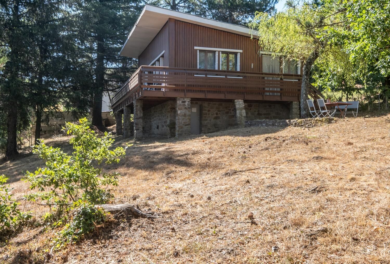 A two-story cabin with a balcony, surrounded by trees and dry grass.
