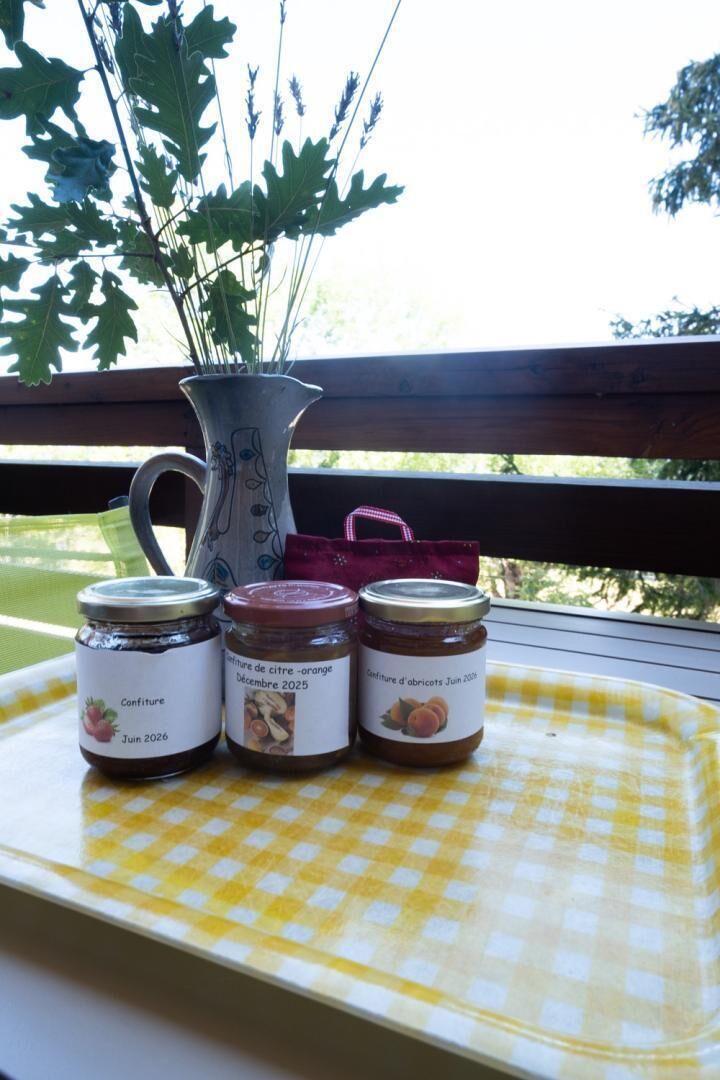 A checkered tray with three jars of jam and a decorative pitcher on a balcony.