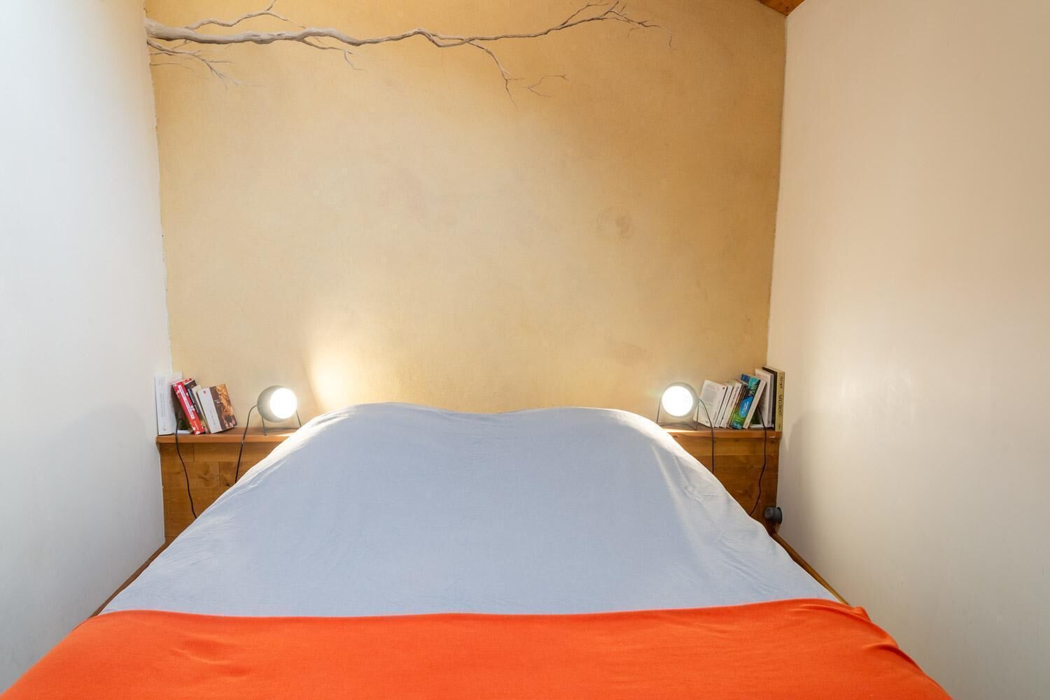 A narrow room with a bed, two bedside tables with lamps, and bookshelves.